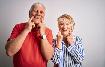 Senior broadly smiling couple pointing at their nice teeth.
